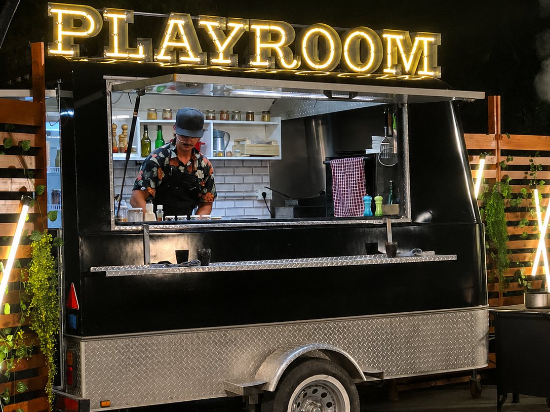 Food truck negro de OCHO de noche, con un cartel luminoso sobre el techo y un cocinero trabajando en la ventana de atención