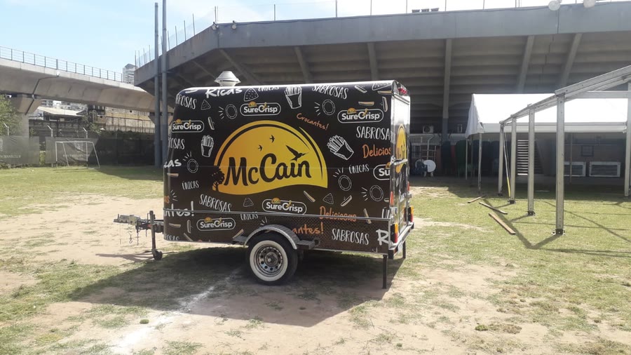 Trailer de OCHO ploteado con la gráfica de una marca de alimentos congelados, sobre el césped de un predio con tribuna